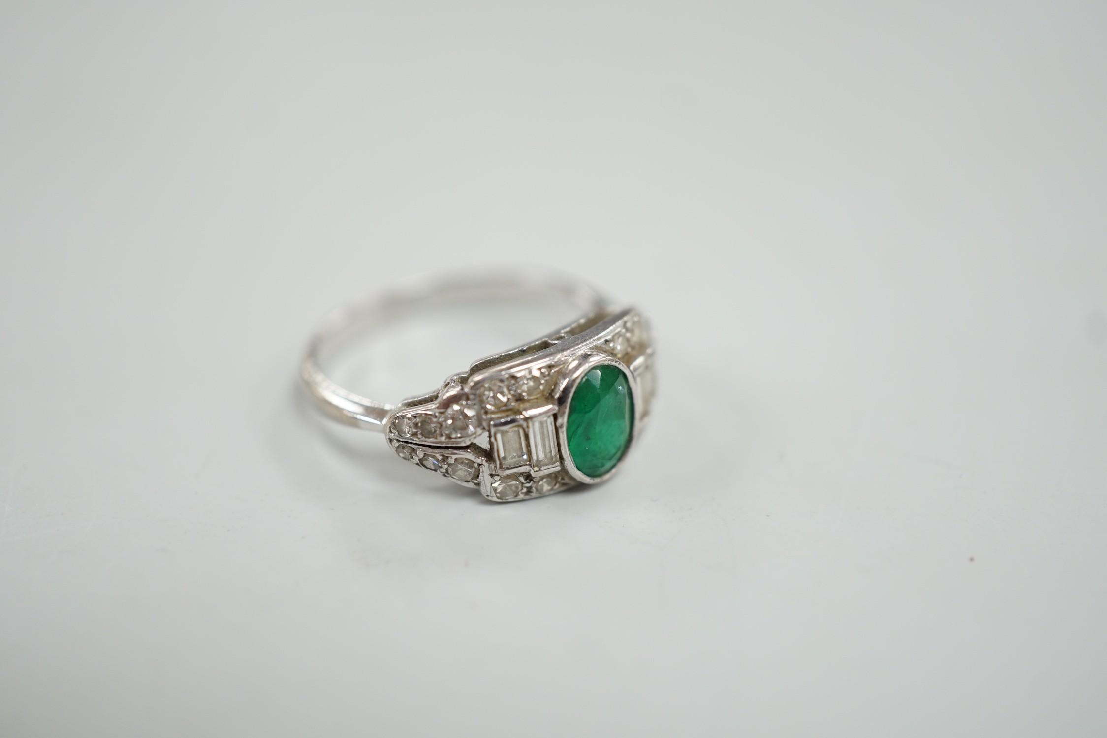 An Art Deco white metal, singe stone oval cut emerald and round and baguette cut diamond cluster set ring, size O/P, gross weight 4.2 grams.